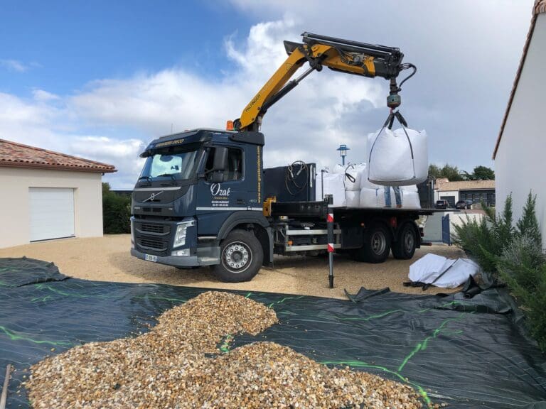 Camion Ozaé effectuant une livraison de graviers en big bag, avec bras de grue, pour l’aménagement d’une cour gravillonnée.